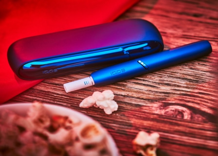 Stellar blue IQOS 3 Duo holder and charger with HEETS stick on a table next to popcorn