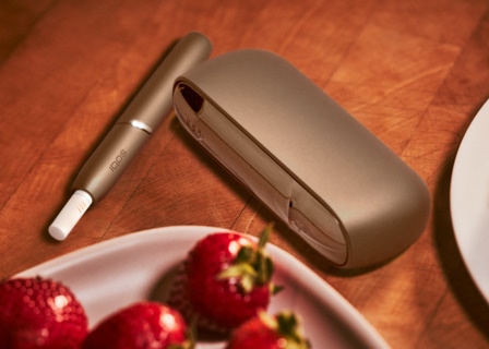 Brilliant gold IQOS 3 DUO holder with HEETS stick and charger next to a plate of strawberries