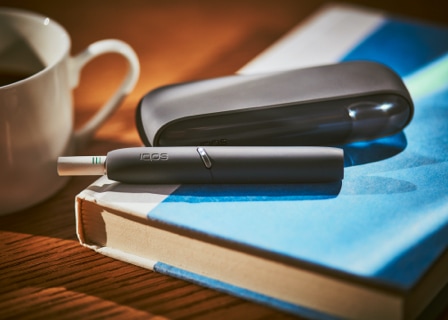 Black IQOS 3 DUO holder with HEETS stick and charger on a book