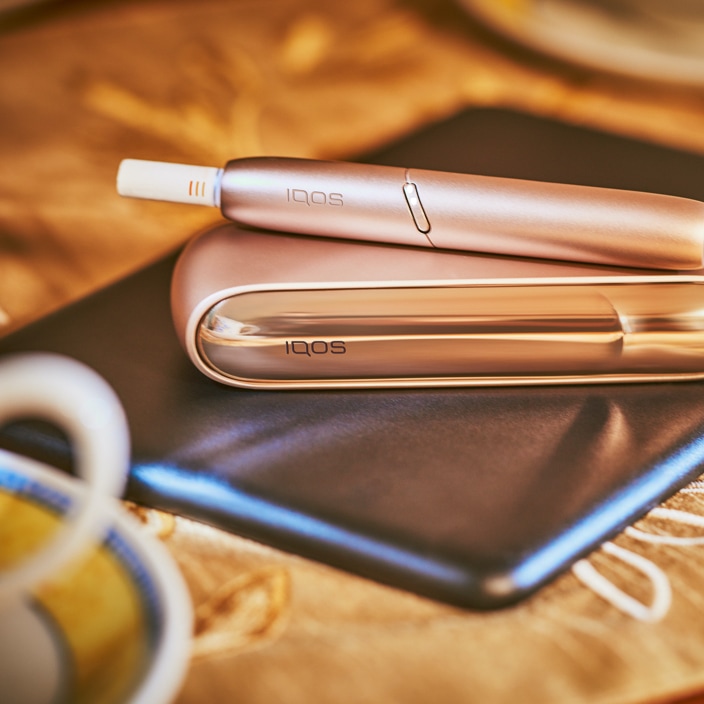 Brilliant gold IQOS 3 DUO with HEETS stick on top of charger